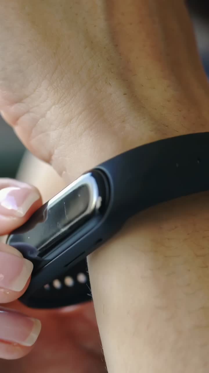 Vertical video: Lifting tracker module, hand sliding it into black band on wrist, securing at home