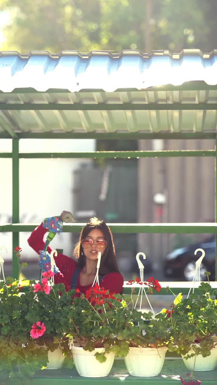 mujer regando cestas colgantes de flores en un mercado