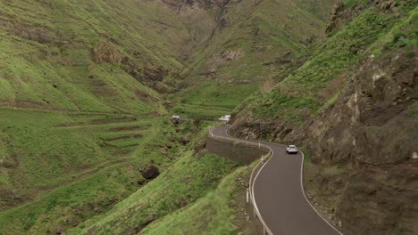 Drone-shot-of-a-car-driving-on-a-road-in-a-green-canyon