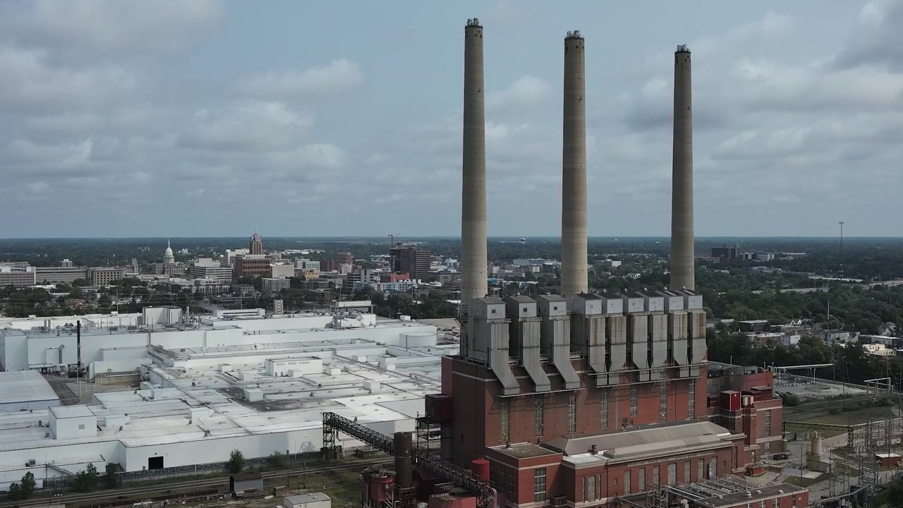 Aerial drone view moving toward Lansing Michigan with the General Motors manufacturing complex and industrial smokestacks visible across the city landscape