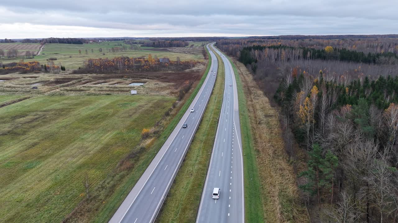 High-altitude tracking aerial view of Lithuania A2 highway. Cars travel through rural autumn landscape between Vilnius and Kaunas