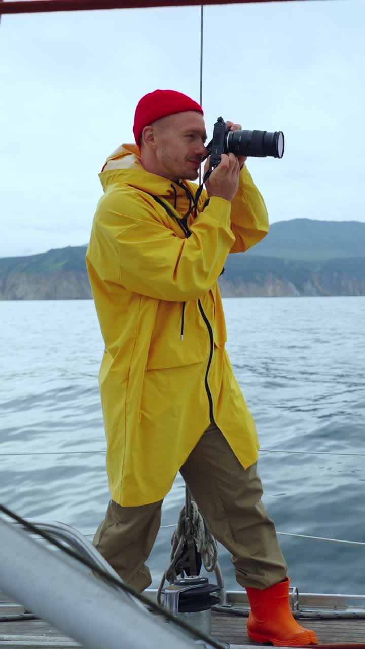 Man in Yellow Raincoat Taking Photos on a Sailboat at Sea