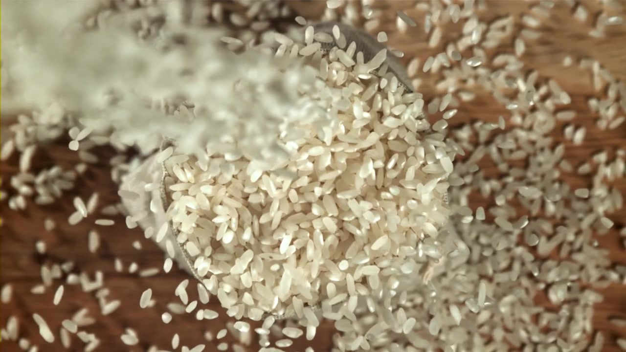Hvide risgryn falder ned i en jutesæk i slowmotion