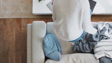 overhead shot looking down on woman at home lying on sofa watching television