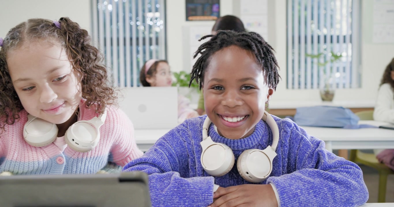 African American schoolgirls working on laptop at front desk while teacher moving back sparking joy