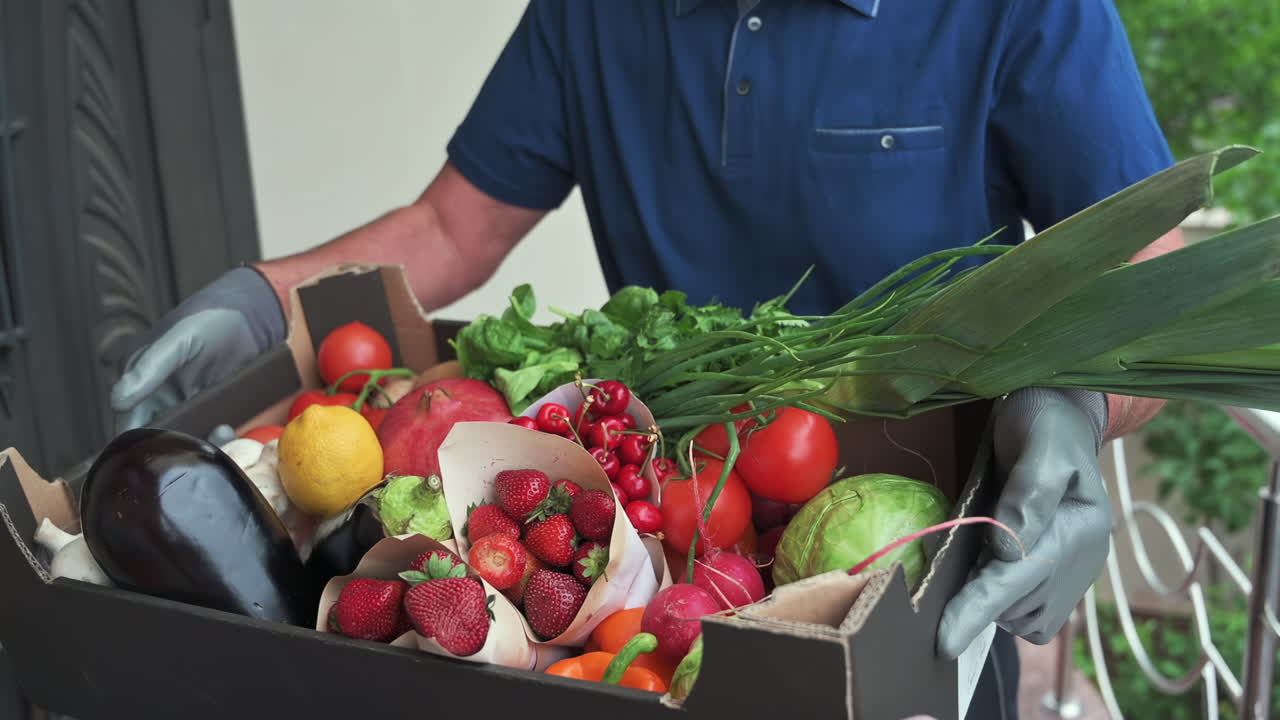 Close up of a man wearing gloves holding a box full of fresh fruits and vegetables