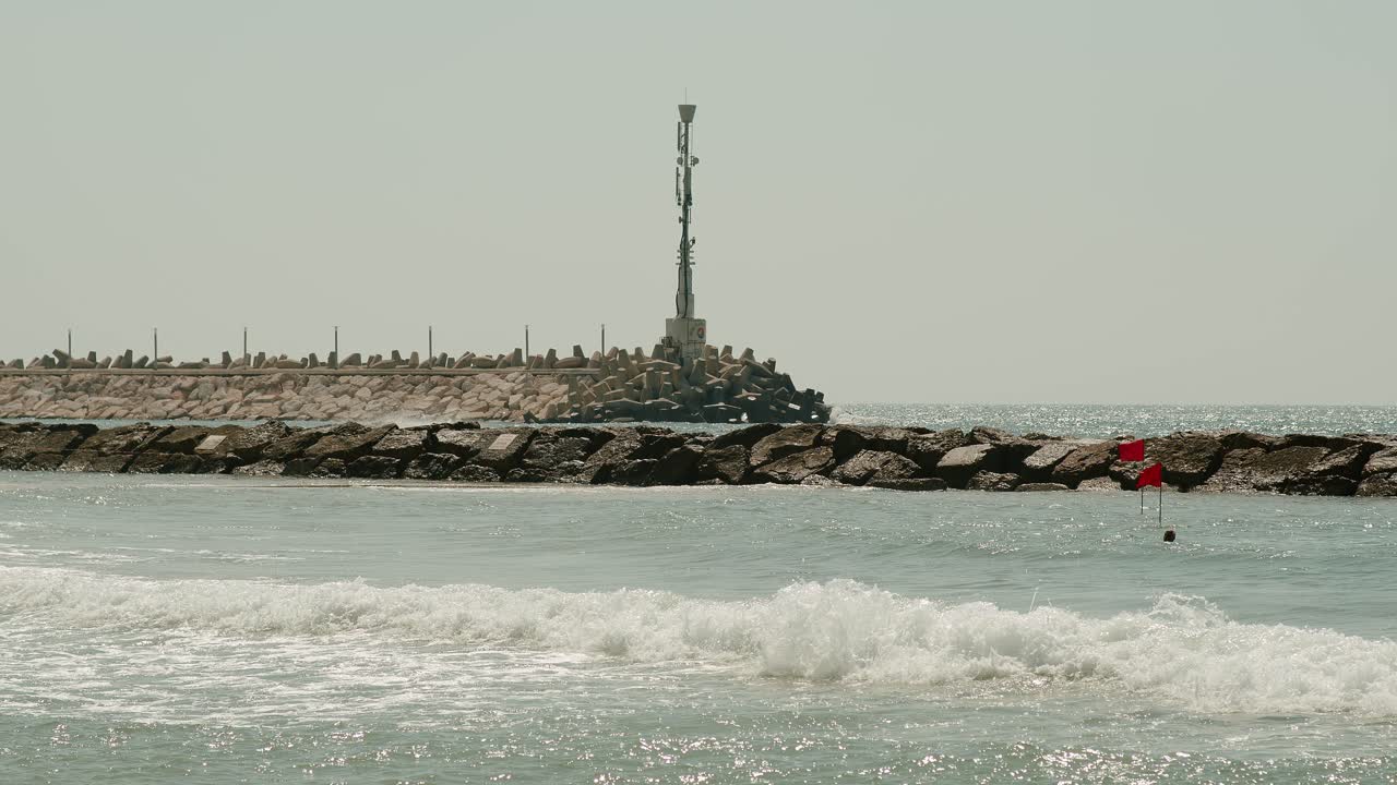 un hombre nada junto al rompeolas con una enorme antena encima de él mientras las olas golpean con fuerza de manera arriesgada