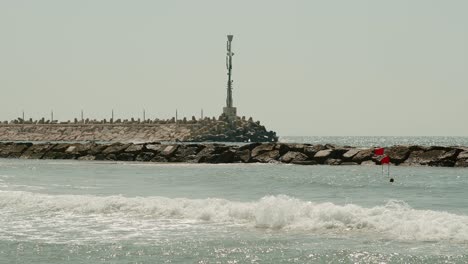 un hombre nada junto al rompeolas con una enorme antena encima de él mientras las olas golpean con fuerza de manera arriesgada