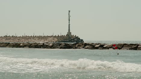 a man swims next to the breakwater with a huge antenna on top of him as the waves hit hard in a risky manner