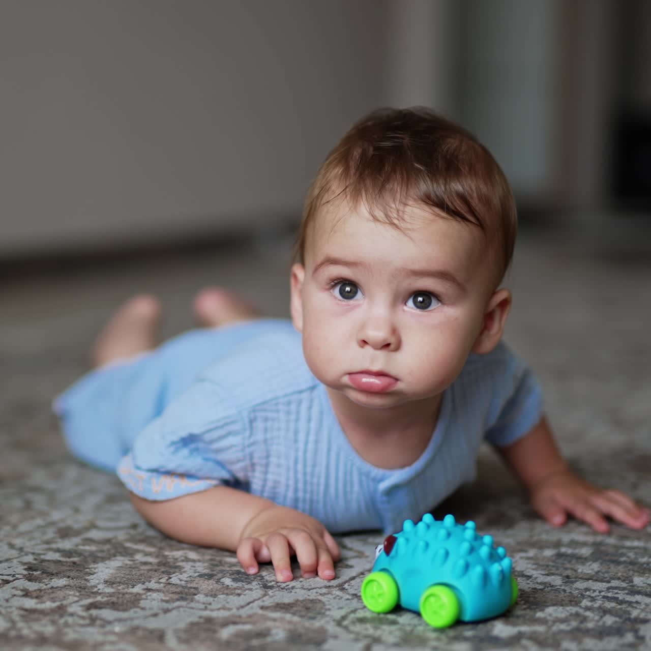 Adorable baby boy lies on the carpet with a toy in front of him. Focused little boy crawls closer to the camera. Close up