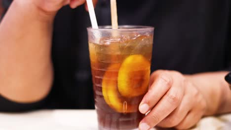 hands stirring iced tea with lemon slices