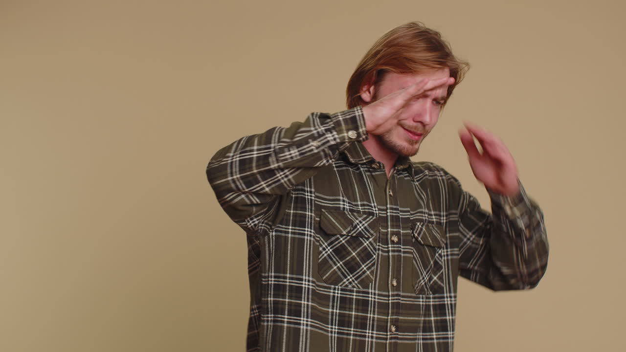 충격을 받은 젊은 성인 남자가 눈을 감고 손을 보이며 멈추는 몸짓을 하고, 혼란스럽고 수줍어하며, 보는 것을 두려워합니다.