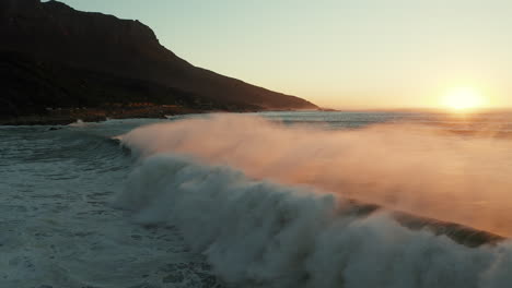 olas rompiendo a lo largo de la costa de una playa durante la puesta de sol en ciudad del cabo, sudáfrica - toma amplia