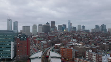 Aerial-ascending-footage-of-subway-leaving-overground-station.-Revealing-cityscape-with-high-rise-buildings-in-background.-Boston,-USA