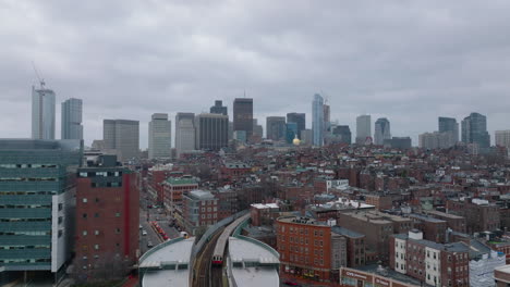 Aufsteigende-Luftaufnahmen-Der-U-Bahn,-Die-Den-Oberirdischen-Bahnhof-Verlässt.-Aufschlussreiches-Stadtbild-Mit-Hochhäusern-Im-Hintergrund.-Boston,-USA