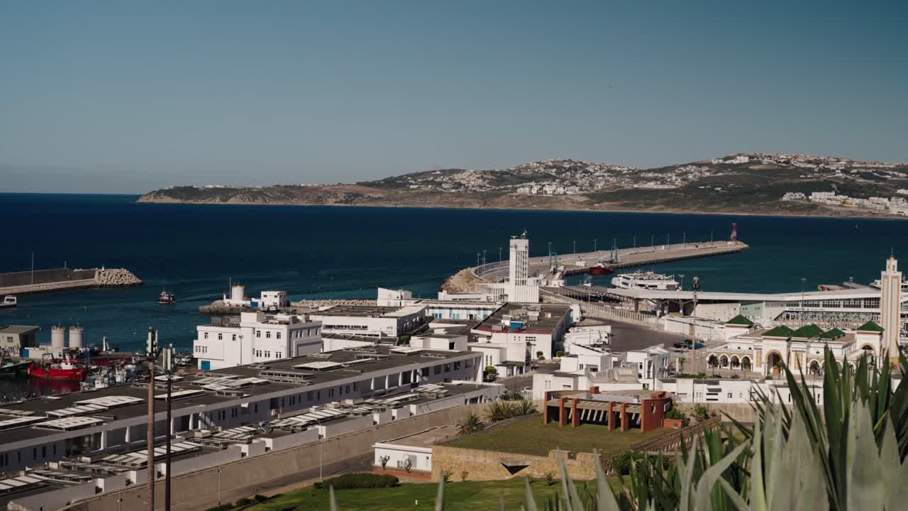 The port of Tangier with white buildings, docks, and the coastline in the background, overlooking the Strait of Gibraltar