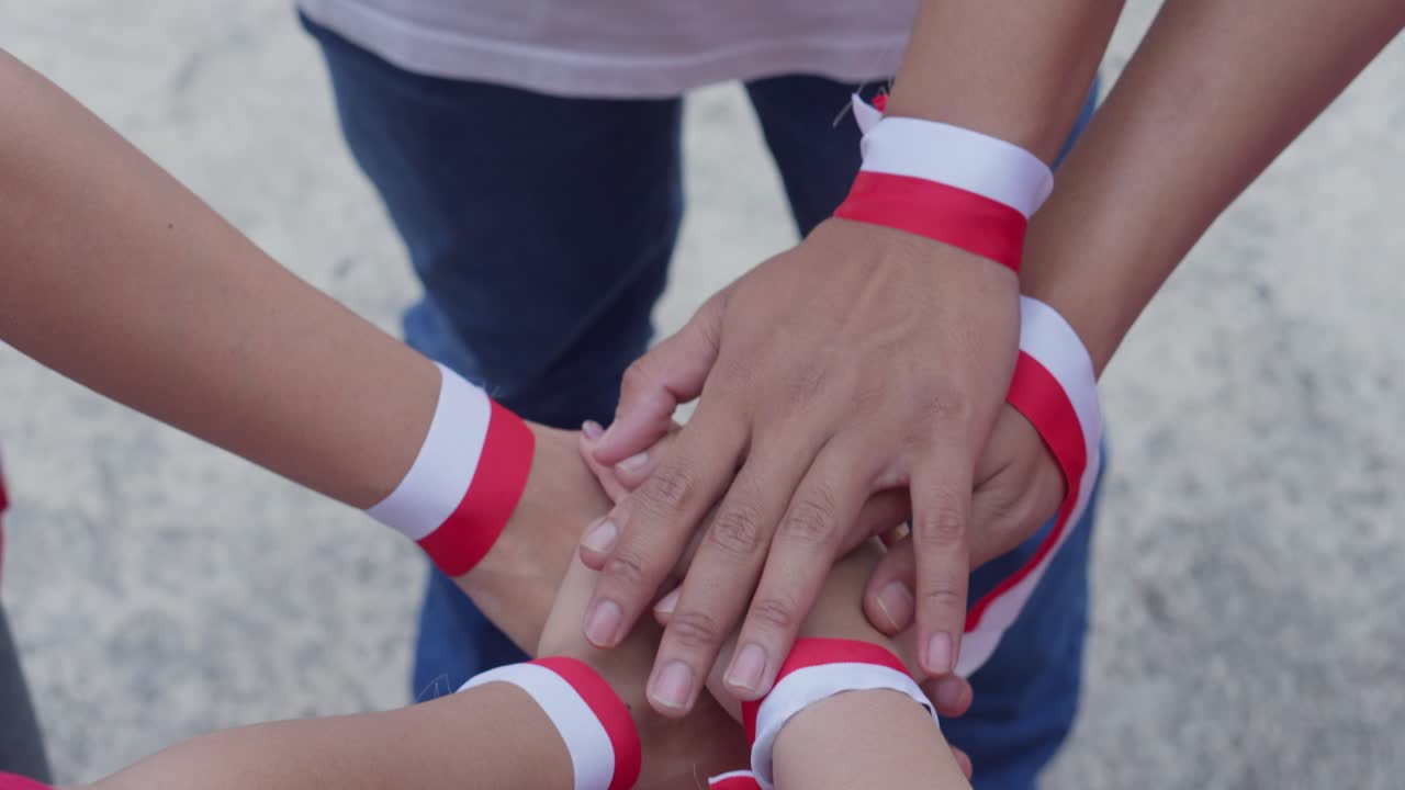 Giovani che uniscono le mani indossando un nastro rosso e bianco indonesiano al polso