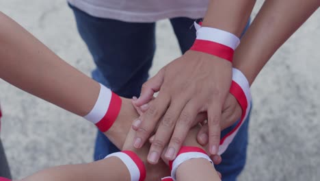 Young-People-Putting-Their-Hands-Together-Wearing-Indonesian-Red-And-White-Ribbon-On-Wrist