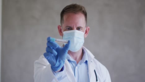 médico caucásico con máscara facial y vacuna en la mano