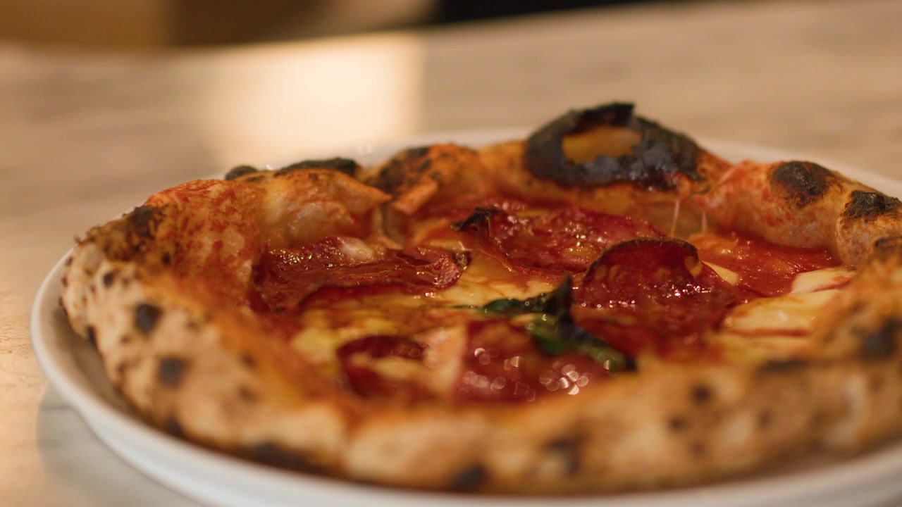 Una mano prende una pizza al lievito madre con pepperoni da un tavolo di marmo con illuminazione soffusa.