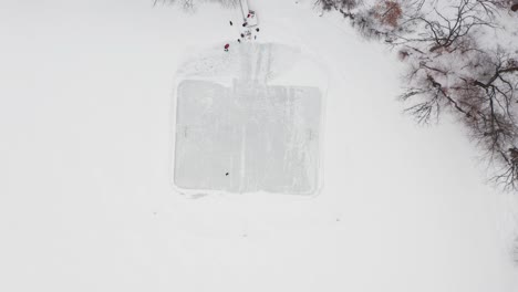 aerial top down, two people skating on ice hockey rink made on frozen lake