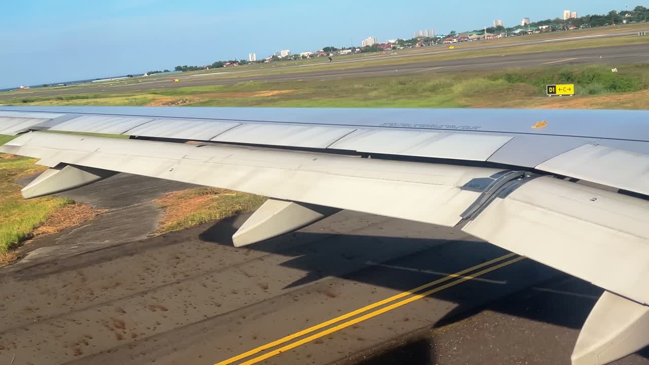 Wide-angle shot of a jet wing taxiing on a sunny runway with grass fields and city skyline—ideal for aviation and travel storytelling
