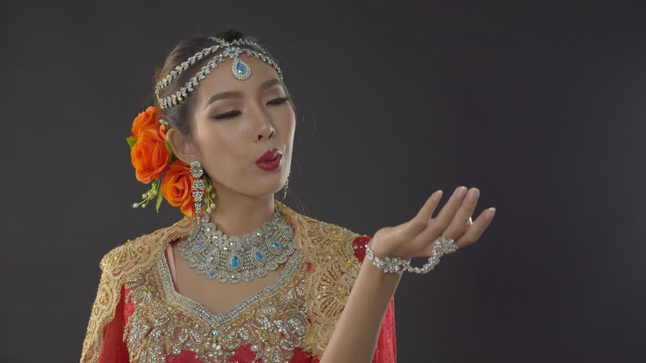 Stunning bride in traditional Indian wedding dress, makeup and jewelry blows a kiss to the groom who is out of frame