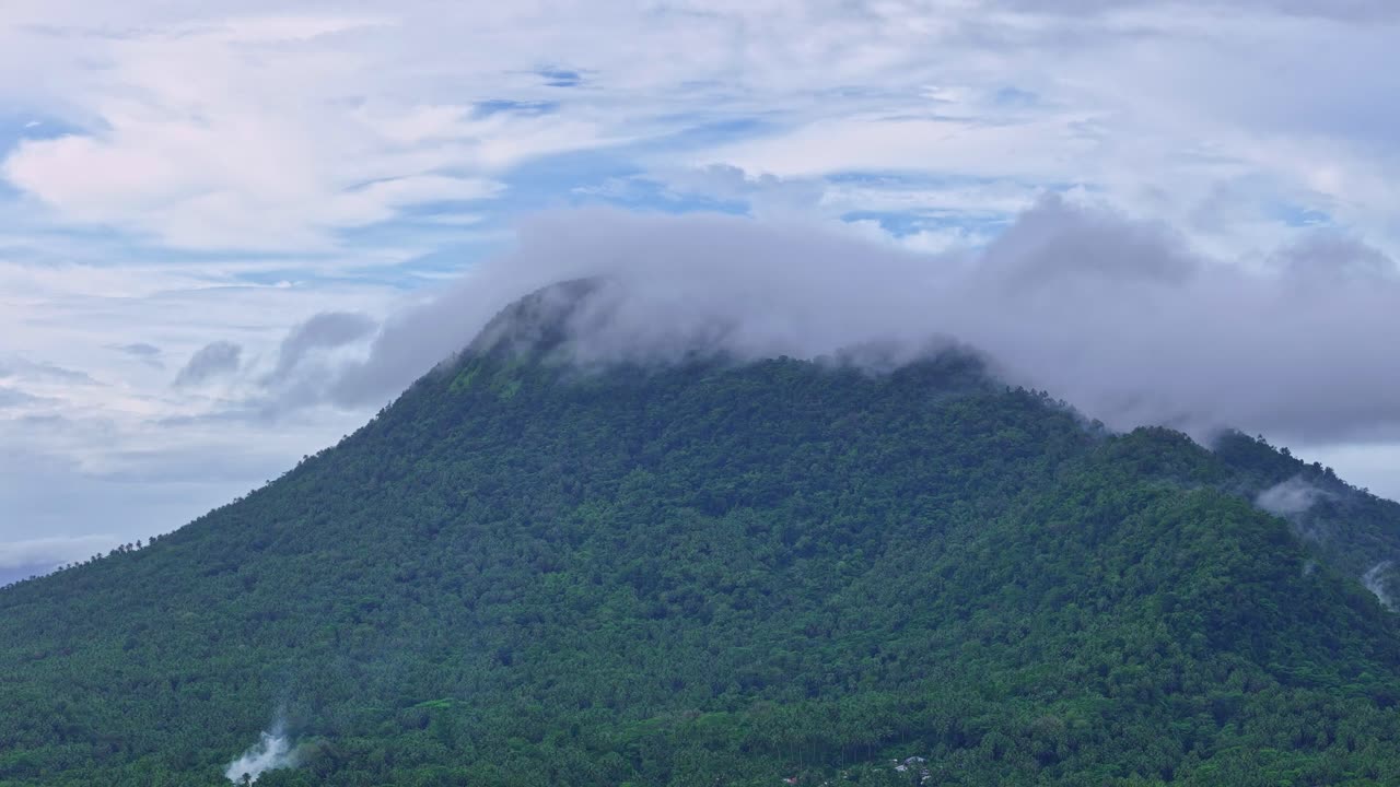 Rekaman video drone udara dari Gunung Paco di Surigao del Norte, Filipina, yang menampilkan medan pegunungan yang diselimuti awan dan lereng berhutan. Lanskap alam yang diambil dari atas dalam kondisi mendung