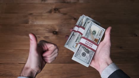 male hands hold three stacks of 10000 us dollar bills and show thumb up sign