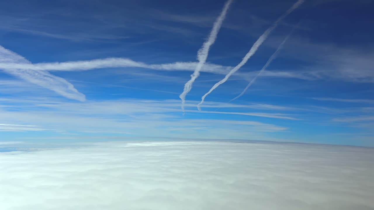 An immersive cockpit view recorded from the cockpit of a jet while flying over an endless sea of fluffy white clouds, with many contrails in a deep blue sky