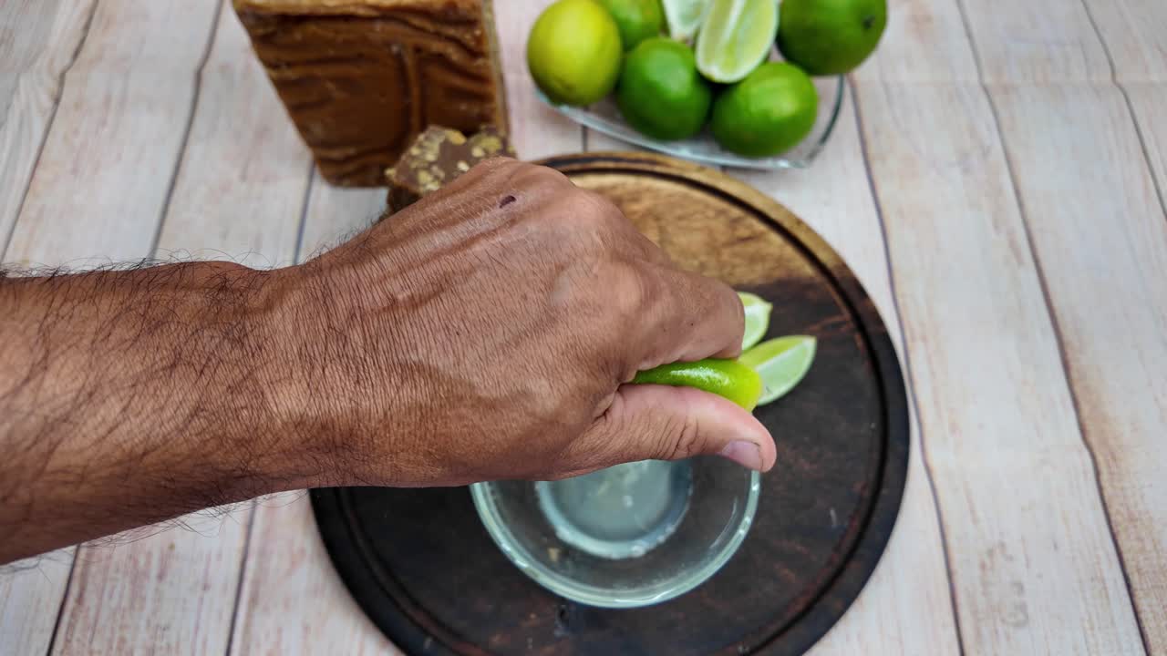 Hands squeeze fresh lime into glass container mixing sweet and citrus notes for a traditional refresher drink papelon con limon