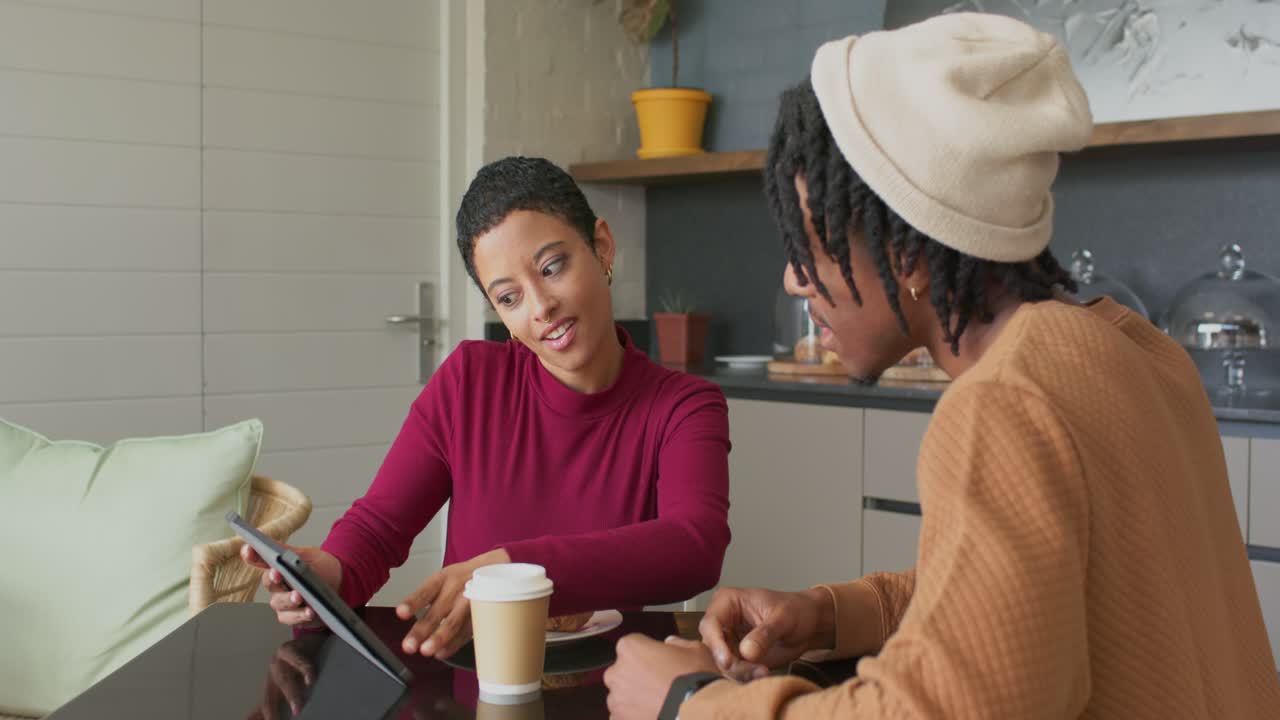 Diverse coworkers collaborating at modern cafe, touching and lifting tablet, sharing design ideas
