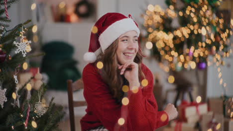 Mujer-Alegre-Con-Sombrero-De-Papá-Noel-Sentada-Con-La-Mano-En-La-Barbilla-En-Una-Casa-Decorada