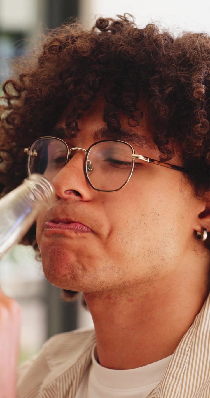 Young Man With Curly Hair Drinking From A Glass Bottle