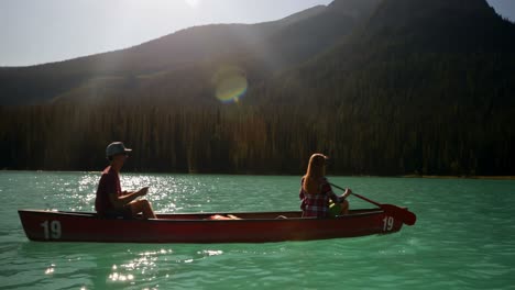 Side-view-of-young-couple-rowing-boat-on-a-turquoise-river-4k