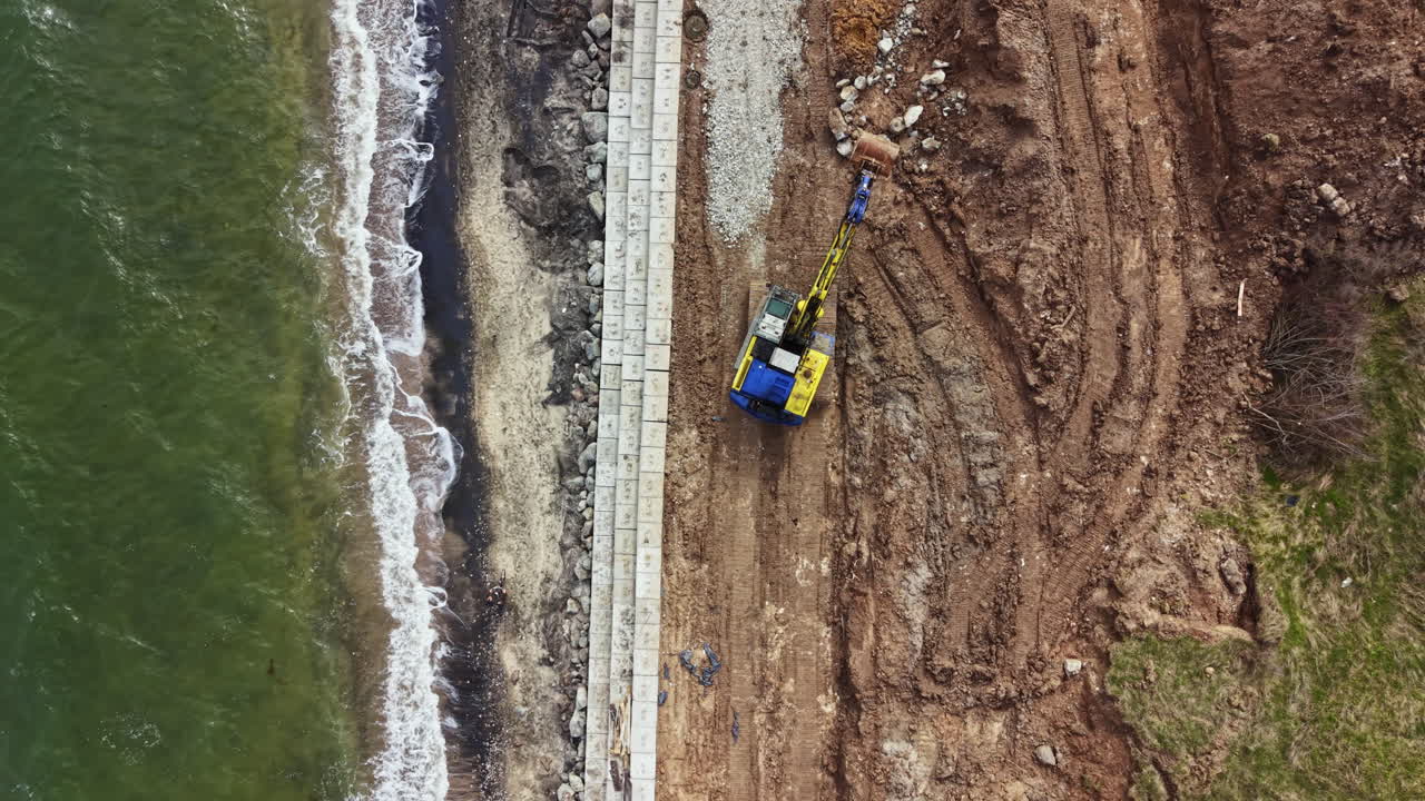 Lavori di costruzione si svolgono sulla riva con macchinari pesanti vicino all'acqua durante il giorno