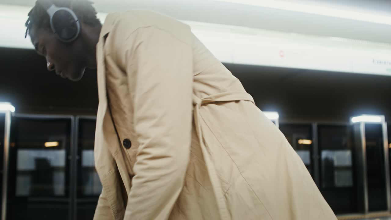 Man in trench coat wearing headphones at a subway station