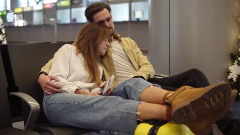 tired young caucasian couple sitting and trying to sleep in departure lounge with suitcase and waiting for delayed flight