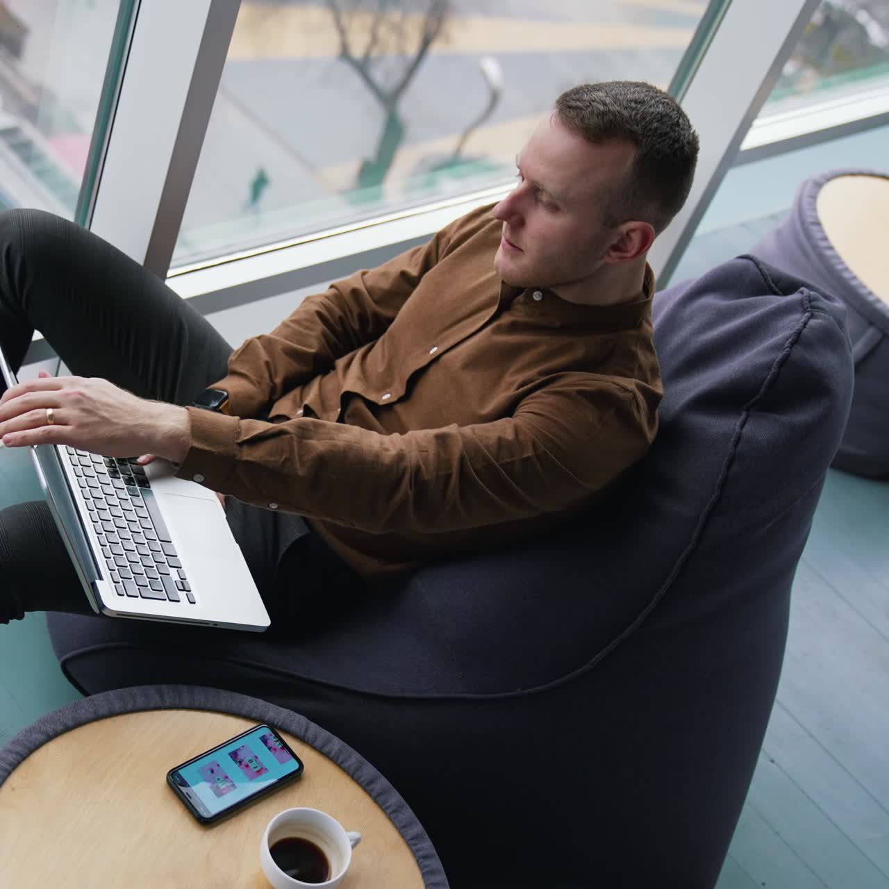 Tired businessman is having a break. Young man closes the laptop and looking through the window on a city landscape. Freelancer works in comfortable place