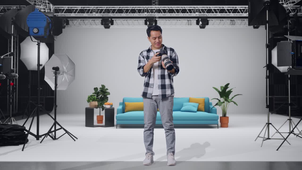 Full Body Of Asian Photographer Looking At The Pictures In The Camera And Smiling Being Satisfied With The Result While Standing In The Studio