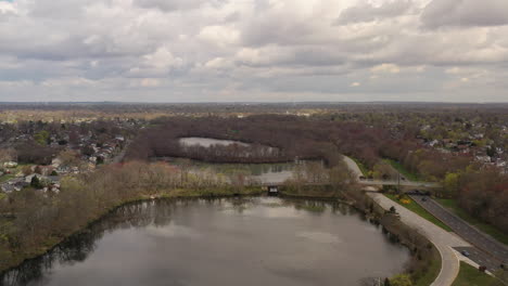 A-high-angle-drone-view-over-a-quiet-lake,-surrounded-by-dry,-brown-trees-and-a-road