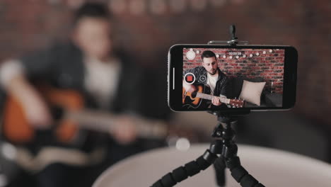 joven músico masculino transmitiendo un video tutorial sobre tocar la guitarra en casa