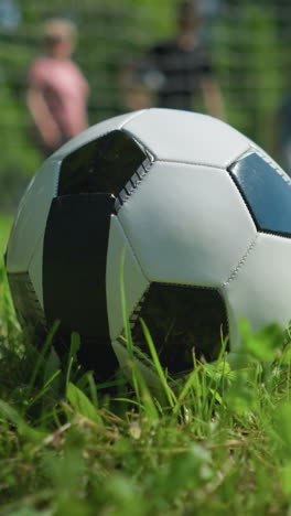 vista de primer plano de una pelota de fútbol descansando en un campo de hierba con una vista borrosa de personas caminando en el fondo