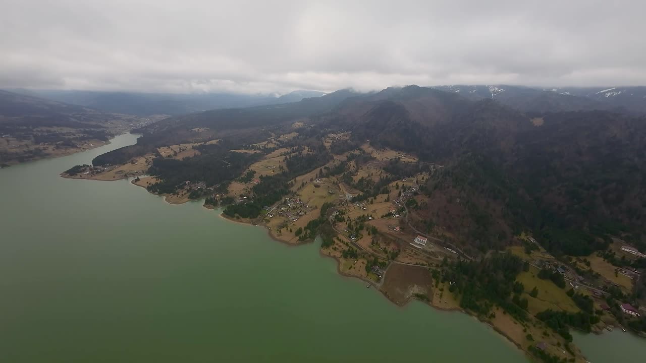 트란실바니아, 루마니아에서 구름이 많은 날에 산란한 시골 집들과 함께 숲이 인 언덕을 따라 멋진 콜리비타 호수의 공중 풍경