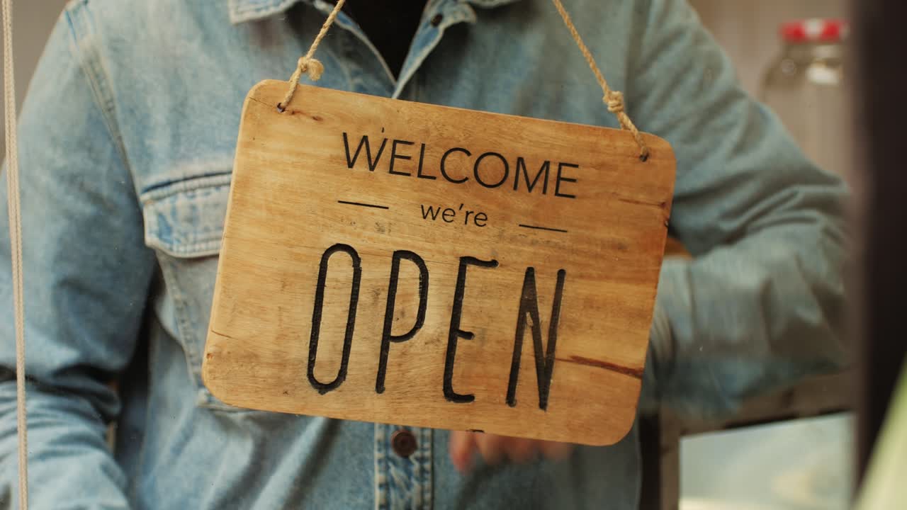 Young man worker flipping sign closed to open close-up. Turn sign to open at the beginning of day. Worker opening cafe, restaurant or shop. Small business development concept.