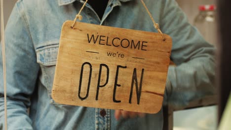 young man worker flipping sign closed to open close-up. turn sign to open at the beginning of day. worker opening cafe, restaurant or shop. small business development concept.