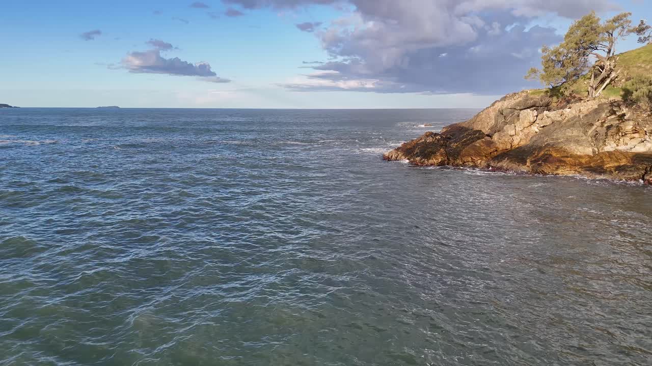 Tranquil ocean waves gently lap against rocky shores under a clear sky at Charlesworth Bay Beach, Coffs Harbour
