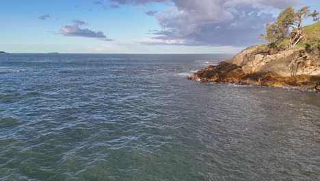 tranquil ocean waves gently lap against rocky shores under a clear sky at charlesworth bay beach, coffs harbour