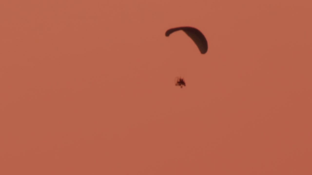Un paramotore scivola dolcemente in un cielo dai toni caldi al tramonto