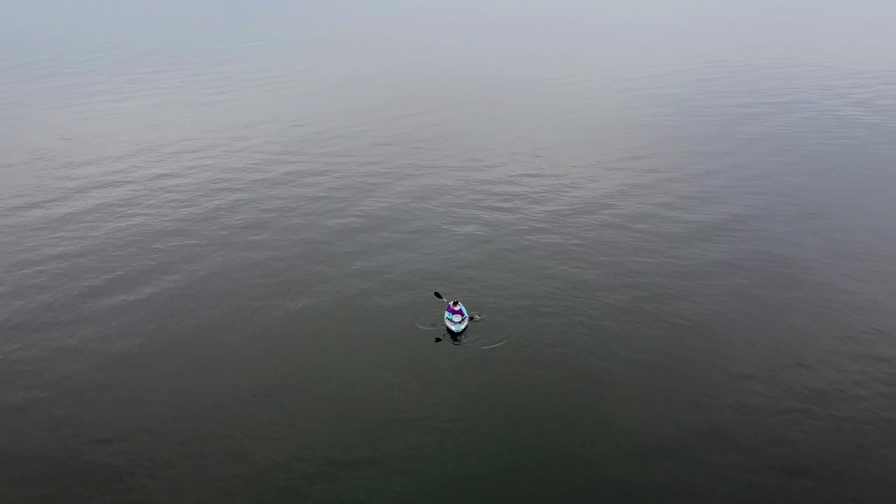 drone aéreo dispara a una chica en un kayak remando en un día nublado
